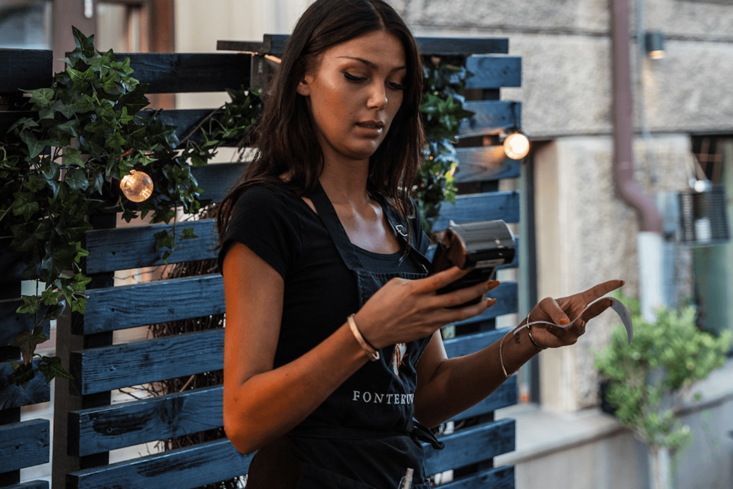 Pergola — server taking a card payment on a portable terminal by the greenery