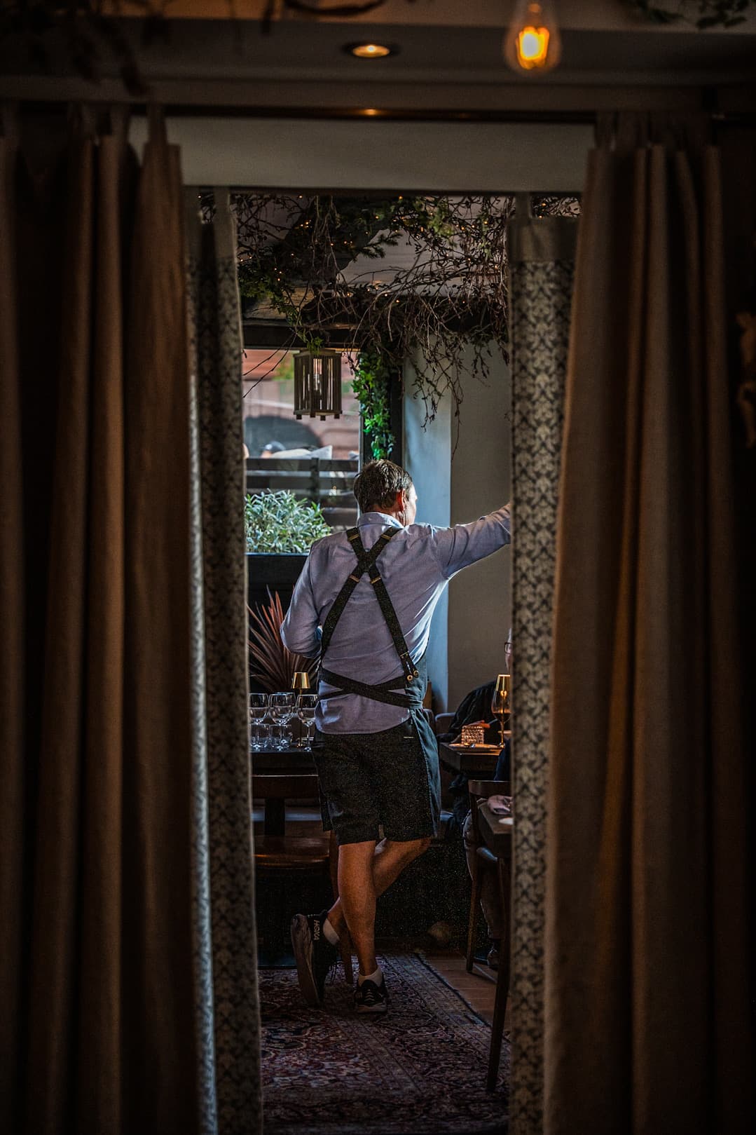 A server in the doorway between the curtains, looking out to the terrace