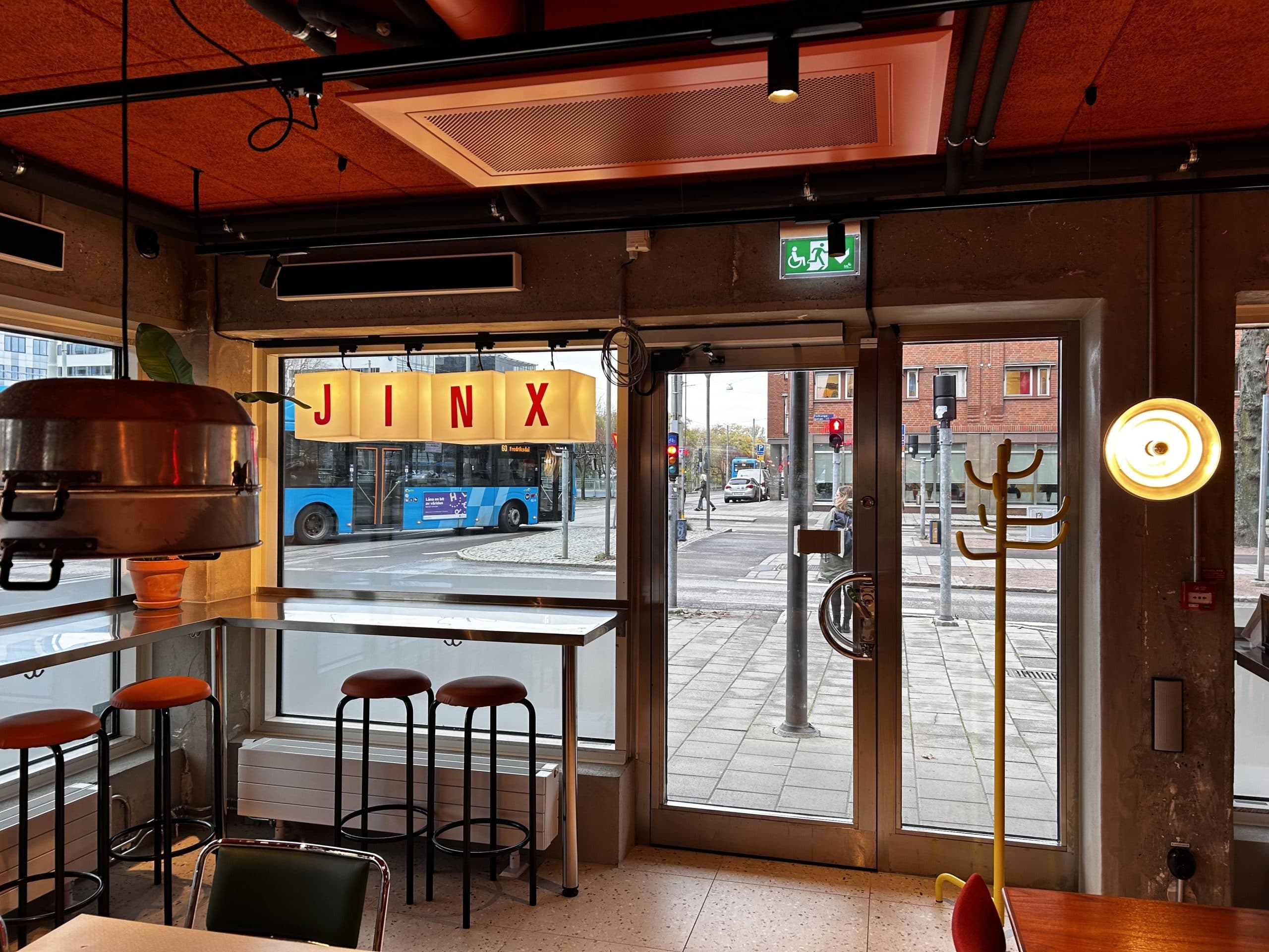 Inside Jinx — the lit JINX sign in the window, bar stools, the street outside